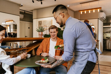 Young asian waiter serving customers in cafe