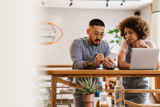 Two business owners discussing work details and using laptop while standing in cafe