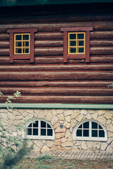 Fototapeta na wymiar The facade of the building has four windows. One part is made of logs with window frames, the lower part is made of stone. Architectural structure and design. High quality photo