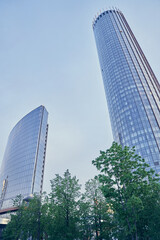 Obraz premium Diagonal modern skyscrapers through the green grass. Mirrored skyscrapers of the business center on a summer day against the blue sky. High quality photo