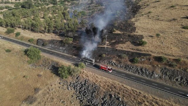 Firetruck with water hose next to a burning passenger bus, drone pulling away