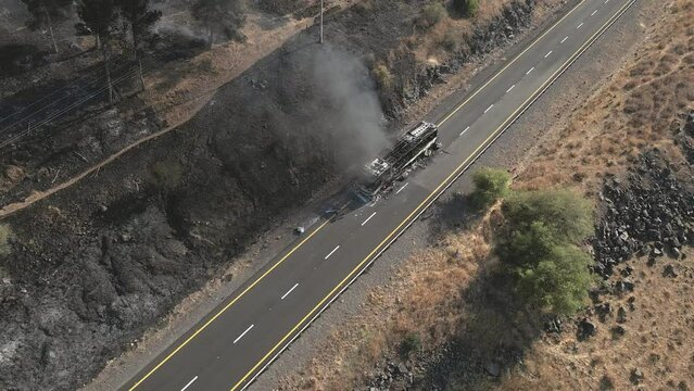Top view, burning passenger bus on side of road and brush fire in countryside