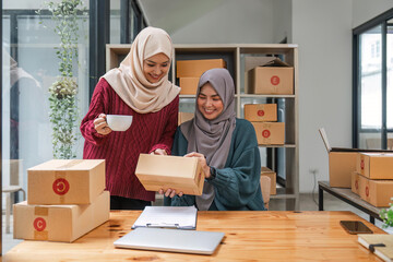 Fototapeta na wymiar Friend muslim female work independent business sme online shopping working on laptop computer with parcel box on desk at home, SME online business and delivery concept