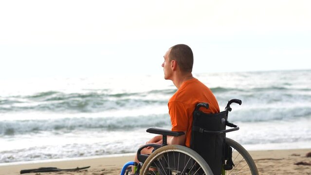 Portrait a disabled person on his back in a wheelchair on the beach with open arms enjoying the freedom of the sea and nature