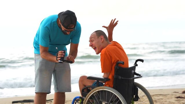A disabled person in a wheelchair on the beach having fun with a friend and a video camera, taking a selfie