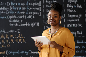 Portrait of African American teacher smiling at camera while using digital tablet at lesson...