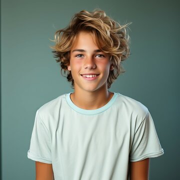 Portrait of a happy smiling teen boy with blond hair. Closeup face of handsome teenage boy with curly hair smiling at camera on a greenish background. Front view, teenager boy in a shirt with a smile.