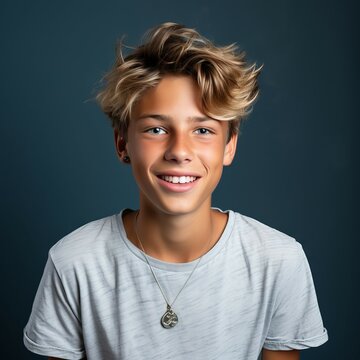 Portrait of a happy smiling teen boy with blond hair. Closeup face of a handsome teenage boy with curly hair smiling at camera on blue background. Front view, teenager boy in a blue shirt with a smile