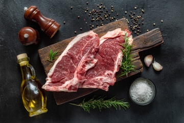 Fresh beef raw steak on wooden board with spices on dark stone background top view