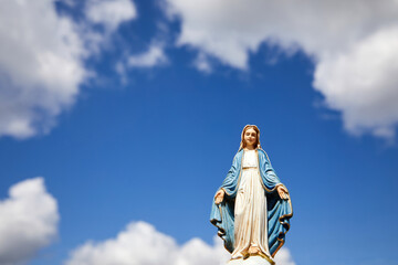 Assumptio of Mary. Virgin Mary statue with the blue sky with white clouds. - obrazy, fototapety, plakaty
