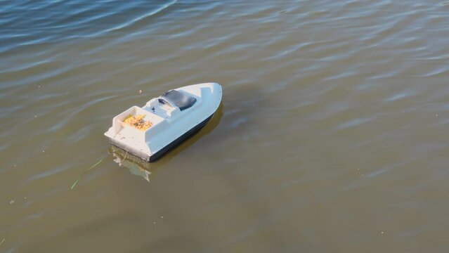 Fisherman imports bait by boat on lake for fishing carp. A GPS boat loaded with corn is looking for fish using a fathometer. Wireless remote fish finder boat on water carries fishing feeder. 4K 25FPS