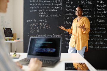 African American teacher standing at blackboard and teaching students IT at class