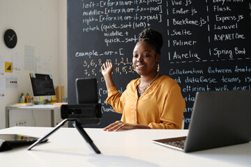 African American teacher leading her blog online about IT while sitting at table in front of...