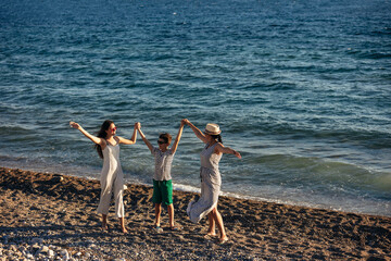 Mother and children holding hands enjoying the sunset on the beach. Happy family travel and vacation concept.