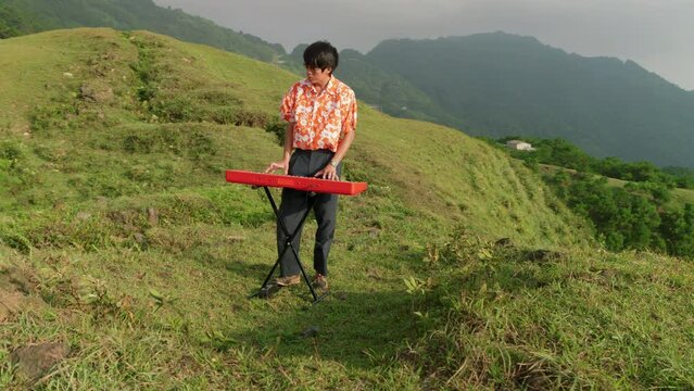 Handsome man playing synthesizer standing on meadow, at sunset. Romantic, meditation, electronic music