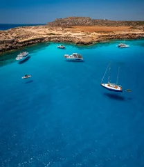 Gordijnen Aerial view of Cavo Greco's mesmerizing blue lagoon in Cyprus. Captured by a drone, the photo showcases the crystal-clear, transparent sea. With its vibrant blue hues and pristine waters © Evgeni