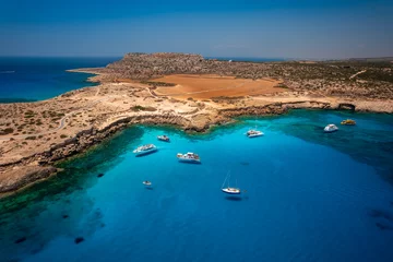 Gordijnen Aerial view of Cavo Greco's mesmerizing blue lagoon in Cyprus. Captured by a drone, the photo showcases the crystal-clear, transparent sea. With its vibrant blue hues and pristine waters © Evgeni