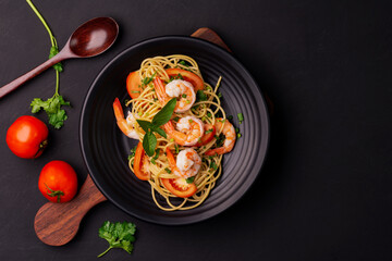 Stir-fried spaghetti or stir-fried noodles Tomato sauce and prawns on a black plate On a wooden table background. Top view.