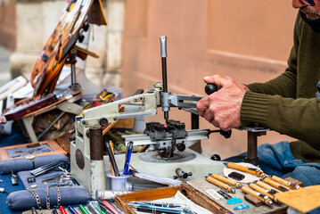 Elderly engraver at work on a street bench. Detail of the hands engrave plaques, pens and other objects. Old jobs.