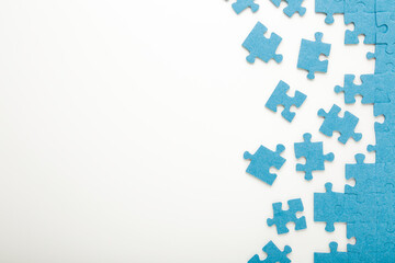 Unfinished blue puzzle pieces on white table background. Closeup. Top down view. Empty place for text.