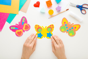 Young adult woman hands holding colorful butterfly shape from paper on white table background....