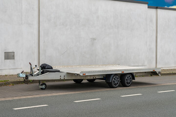 Side view of a platform car trailer standing on the side of the road along a concrete fence.