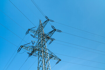 A high-voltage mast with wires stretching towards it against a background of pure blue sky. Bottom view.