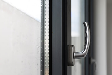 Tilt and turn window handle in a large window in a public building. The window is made of plastic, visible silicone seals.