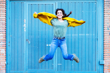 Smiling woman in a yellow coat jumps in front of a blue door