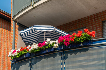 View of the balcony of an apartment building with geranium flowers and a solar umbrella in sunny...