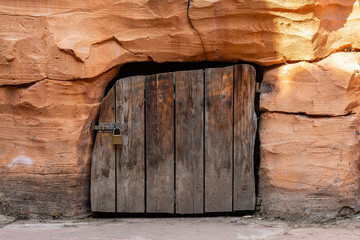 Rough wooden door padlocked in orange stone wall.