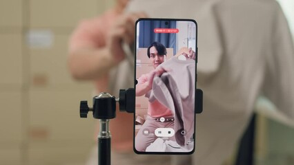 Close up youth Asia male owner small business online shop sit front of phone look at camera live streaming show polo shirt clothing new arrival to follower sale promotion retail online shop at home.