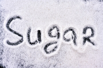 The word sugar is written on a black chalkboard with a bunch of sugar