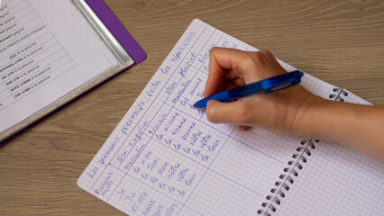 Learning French. The hand writes the grammar of a foreign language in a notebook. New knowledge and education. Photo closeup