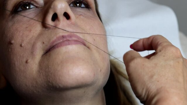 The beautician performs a woman's facial hair removal using the ancient Arabic thread technique. Manual technique popular in many Arab and Asian countries.