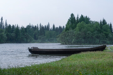 An old wooden boat on the river bank, in the middle of the forest in the morning