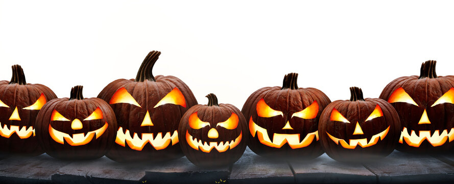 A group of seven lit spooky halloween pumpkins, Jack O Lantern with evil face and eyes on a table isolated against a transparent background.