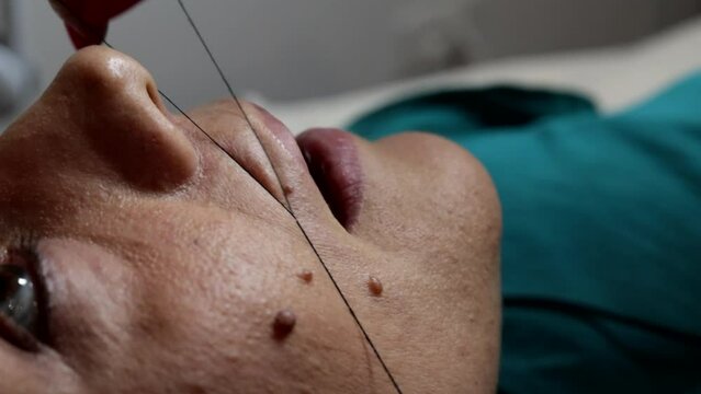 The beautician performs a woman's facial hair removal using the ancient Arabic thread technique. Manual technique popular in many Arab and Asian countries.