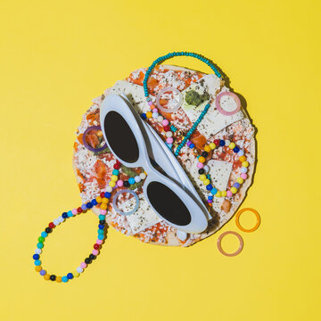 White sunglasses, bright beads and necklaces on pizza in a minimalist style. Creative concept of fashionable food.