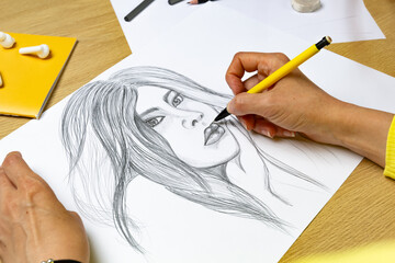 The artist draws a pencil portrait of a young beautiful woman. The designer creates a picture of a girl on white paper.