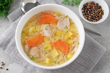 Chicken soup with noodles and vegetables in white bowl on a gray concrete background.