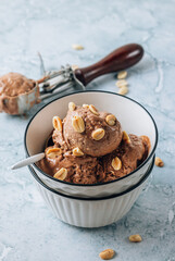 Homemade vegan peanut butter, banana and chocolate ice cream in a bowl with peanuts over gray marble background.