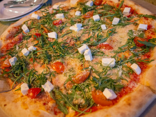 a whole piza with a lot of basils and cheeses on the wooden table of cafe in Kyiv 