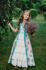 Obraz na płótnie Canvas Pretty little smiling girl with bouquet of heather flowers in long vintage dress standing in summer park with green background, vertical lifestyle outdoor kid's portrait in provence country style