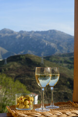 Glasses of dry white wine and spanish tapas olives in bowl with mountains peaks on background in sunny day