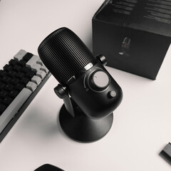 A close - up of the condenser microphone in black on a white background and equipped with a box, keyboard, mouse and earphones for YouTubers and vloggers.