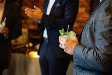 Close up of mojito cocktail in man hand in a business suit with blurred people in the background on...