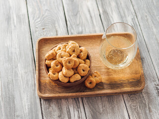 Traditional italian snack taralli or tarallini in wooden bowl and wine glass over wooden tray on old gray wooden background. Rustic shot of taralli appetizer with copy space