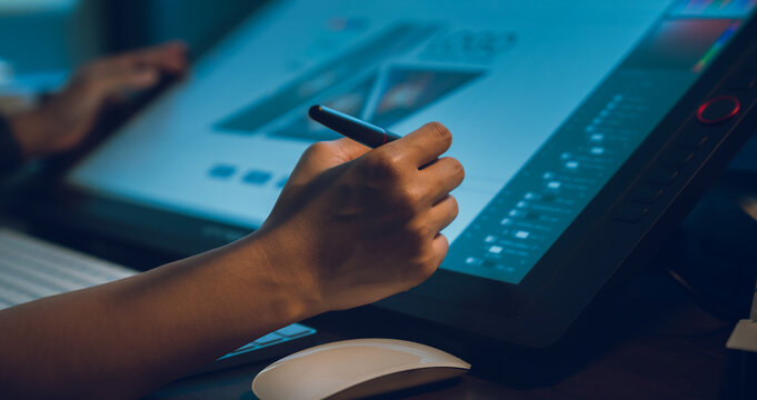 Designer working on the table in home studio and hand using digital pen on monitor screen with editor retouching photos.