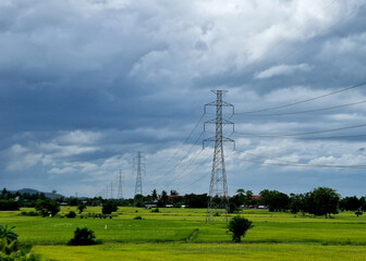 The 230kV transmission line towers on a rice field in the countryside on clouds in the blue sky...